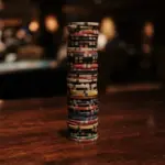 A tall, precisely stacked column of diverse casino chips rests on a dark, polished wooden table
